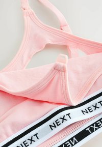 Svijetloružičasti bralet s podesivim trakama, crno-bijeli elastični pojas s natpisom "NEXT" i mekom pamučnom teksturom.