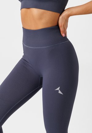 Legginsy o wysokim stanie, prążkowane, w ciemnonawojowym kolorze, z dyskretnym białym logo na dolnej części nogawki oraz gładkim, teksturowanym wykończeniem tkaniny.