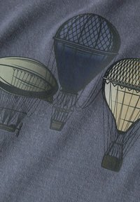Grafikdesign mit drei Heißluftballons in unterschiedlichen Größen, gedruckt auf einem strukturierten dunklen Stoff, mit einer Farbpalette in Blau und Beige.