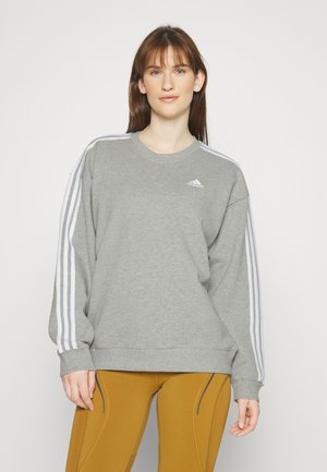Sudadera gris con diseño de tres franjas blancas en las mangas, cuello redondo y puños de canalé. Logo de Adidas en la parte izquierda del pecho.