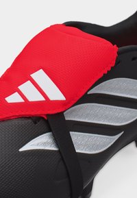 Μαύρο ποδοσφαιρικό παπούτσι με ασημένιες ρίγες και κόκκινο προστατευτικό κάλυμμα με λευκό λογότυπο Adidas πάνω από τα κορδόνια.