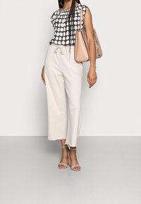 Top blu navy con pois bianchi, pantaloni beige con coulisse e sandali nude con cinturini. Tiene in mano una borsa strutturata rosa chiaro.