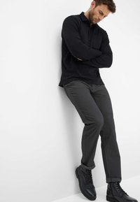 Polo noir à manches longues, pantalon gris ajusté, et bottes noires à lacets. Design simple avec un détail de poche sur la chemise.
