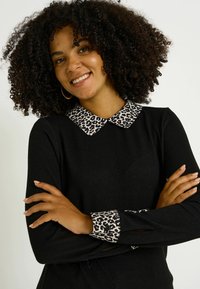 Top negro de manga larga con detalles de cuello y puños de estampado de leopardo, con una textura suave y un diseño ajustado.