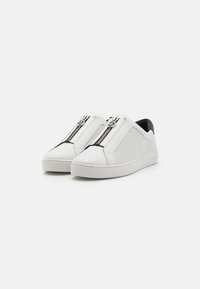 Scarpe bianche slip-on con un pannello in rete, dotate di una cerniera argento e un accento nero sul tallone. Parte superiore in pelle liscia con punta arrotondata.