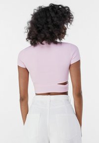 Růžový žebrovaný krátký top s krátkými rukávy a výřezem na zádech. Nosený s bílými kalhotami s vysokým pasem. Hladká textura.