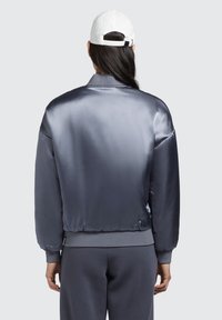 Jachetă bomber din satin de culoare gri închis, cu manșete și tiv cu nervuri, având o textură netedă și o șapcă albă în contrast.