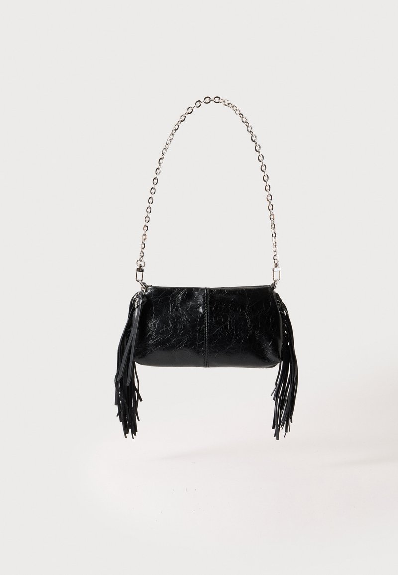 Petit sac à main en cuir noir avec bandoulière chaîne argentée et pompons en cuir noir de chaque côté, sur un fond clair uni.