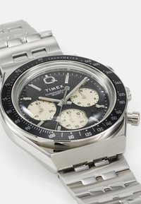 Men's Timex chronograph watch with a stainless steel band, black dial, tachymeter bezel, and cream-colored subdials.