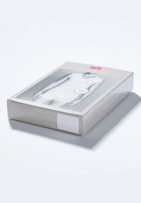 Białe opakowanie koszulki bez rękawów w prostokątnej kartonowej pudełku z szarym tłem, na którym widnieje etykieta "100% Bawełna" oraz szczegóły produktu.