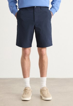 Navy blue cotton shorts with a flat front, side pockets, and a relaxed fit, paired with beige sneakers and white crew socks.