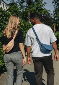 Dvaja jednotlivci kráčajú, jeden s béžovou crossbody taškou a druhý s modrou taškou cez rameno, oblečení v neformálnom čiernom a bielom oblečení.