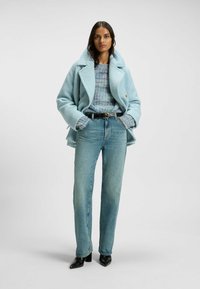 Ljusblå ullblandad kappa med dubbelknäppning, som kombineras med en flerfärgad stickad tröja, högmidjade ljusblå jeans och svarta klackar.