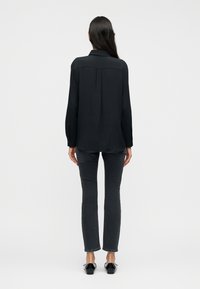 Μαύρο μακρυμάνικο πουκάμισο με γιακά, λεπτομέρεια πτυχώματος στην πλάτη, σε συνδυασμό με σκούρο γκρι εφαρμοστά τζιν και μαύρα μπαλαρίνες. Ομαλή υφή υφάσματος.