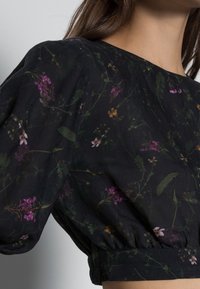 Top in tessuto nero con motivi floreali in viola, giallo e verde. Maniche a palloncino con polsini elasticizzati e vestibilità comoda.