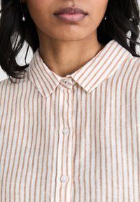 Lightweight, striped shirt in beige and white, featuring a pointed collar, button closure, and a soft, textured fabric.