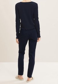 Granatowy prążkowany top z długim rękawem i falowanym dołem w połączeniu z granatowymi spodniami i jasnymi sandałami. Charakteryzuje się dopasowanym krojem i gładką teksturą.