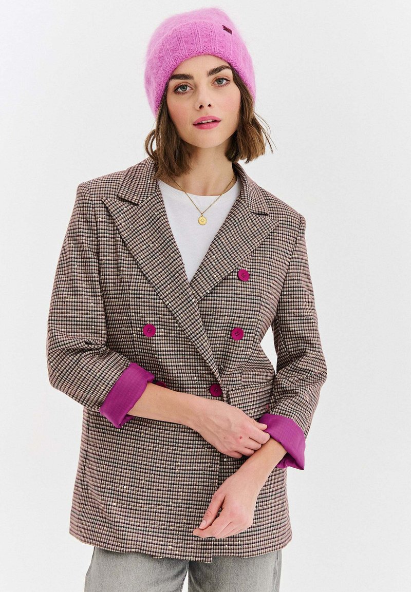 Dvojradové hnedé kockované sako s ružovými gombíkmi a manžetami, nosené cez bielu košeľu, doplnené nadýchanou ružovou čiapkou.