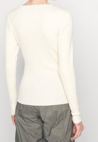 Top lungo a maniche lunghe in crema a coste, con scollatura rotonda e silhouette aderente, abbinato a pantaloni verde oliva larghi e con texture.