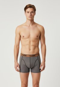 Grå boxershorts med sorte accenter, præget af et prikket mønster. Taljen er brun med "CLAUDIO" trykt i sort.