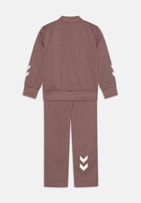 Dres w kolorze dusty rose, wykonany z miękkiego materiału. Kurtka z kołnierzem stójkowym, białe akcenty i wzór w zygzak na spodniach.
