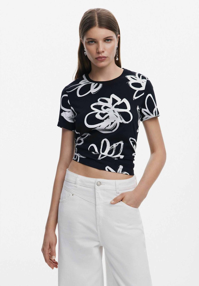Top corto negro con patrón floral blanco, mangas cortas, escote redondo, combinado con pantalones de pierna ancha blancos de cintura alta. Textura de tela suave.