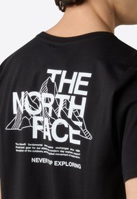 Černé bavlněné tričko s velkým bílým textem "THE NORTH FACE" a grafikou hory, s dalším textem ve spodní části.