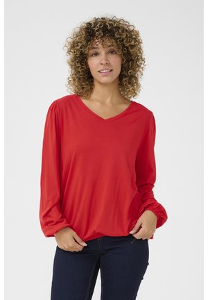 Red long-sleeve top with a V-neck, soft fabric, gathered sleeves, and relaxed fit, paired with dark jeans.