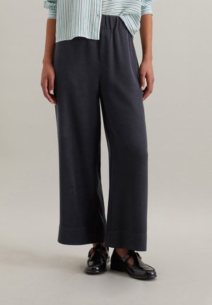 Bredde ben, mørkegrå bukser med elastisk talje og glat tekstur, parret med en lyseblå stribet skjorte med knapper.