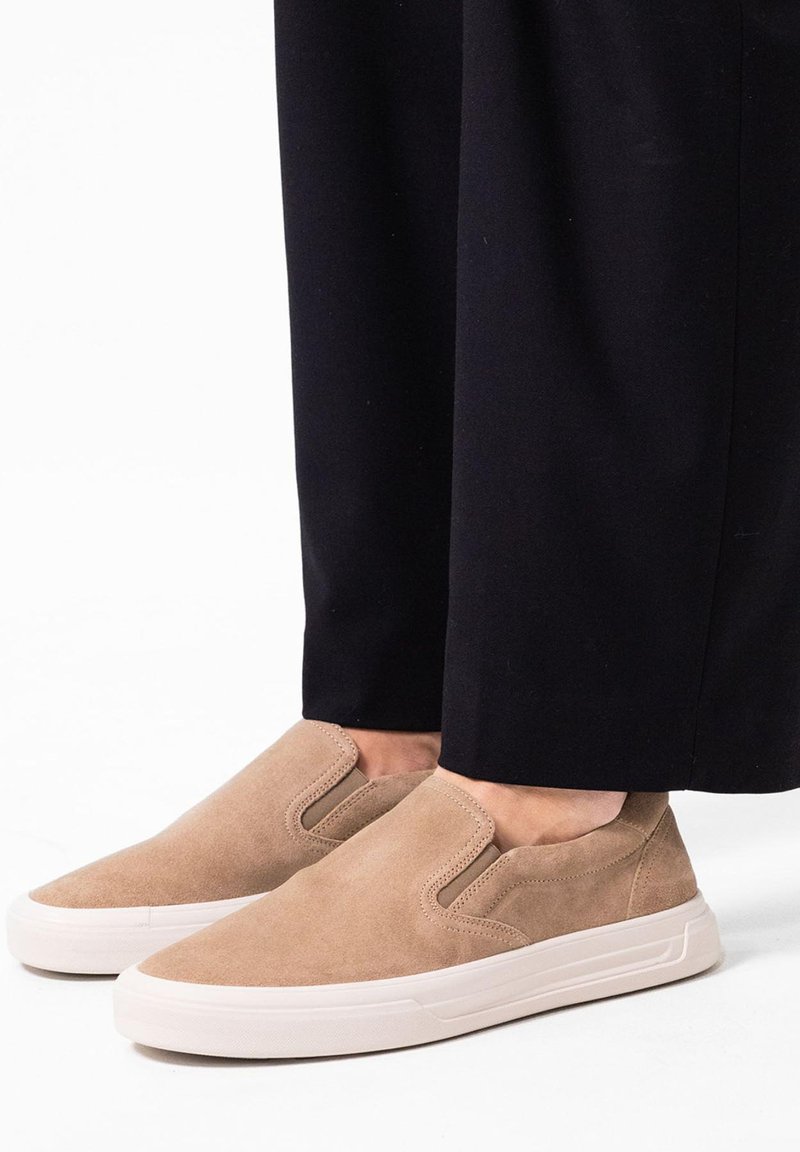Instap schoenen van zacht tan suede met een gladde textuur, voorzien van een elastische zijpaneel en een witte rubberen zool.