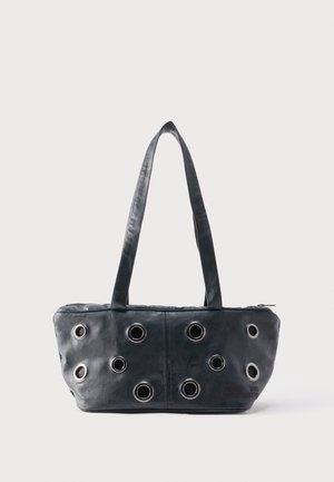 Sac à main en cuir noir avec deux poignées et plusieurs œillets en métal argenté sur le panneau avant, posé sur un fond clair uni.