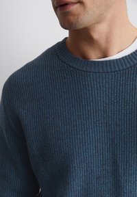 Dunkelblauer, gerippter Pullover mit klassischem Rundhalsausschnitt und strukturiertem Stoff, der eine Mischung aus dunklen und helleren Blautönen highlightet.