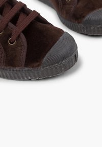 Sneaker in velluto marrone con punte rotonde in gomma e fori per i lacci, caratterizzati da lacci marroni scuri e suole esterne in gomma nera testurizzata.