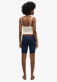 Pantaloni corti blu navy in cotone con orlo arrotolato, abbinati a un top in pizzo crema con spalline sottili e design della schiena aperta.