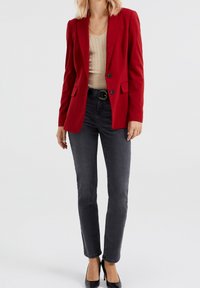 Červený šitý blazer s dvěma předními kapsami, s jedním knoflíkem, spárovaný se svetříkem v světlé béžové barvě s jemným žebrováním a tmavě šedými džíny s vysokým pasem.