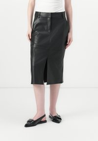 Svart läderpennkjol med framklipp, midjefickor, slät yta och skräddarsydd passform, tillsammans med svarta läder slingbacks.