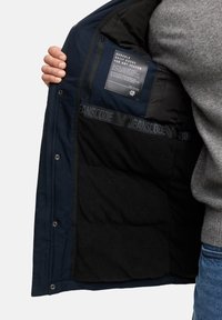 Marine yderjakke med sort fleecefor, udstyret med et mærke og struktureret indre. Trykknaplukninger foran, stilfulde elastiske detaljer.