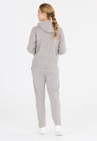 Hellgraue Kapuzenjacke und passende Jogginghose aus einem weichen Baumwollmischgewebe. Verfügt über eine Kapuze und seitliche Taschen, mit gerippten Säumen und Bund.