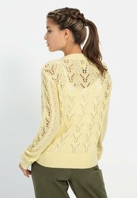 Häkelpullover in Hellgelb mit Zickzackmuster und gerippten Bündchen, offen gearbeitete Details an Ärmeln und Rücken.