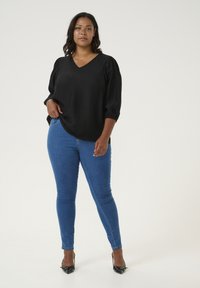 Bluză neagră texturată cu decolteu în V și mâneci bufante, combinată cu blugi skinny blue și pantofi cu vârf ascuțit negri.