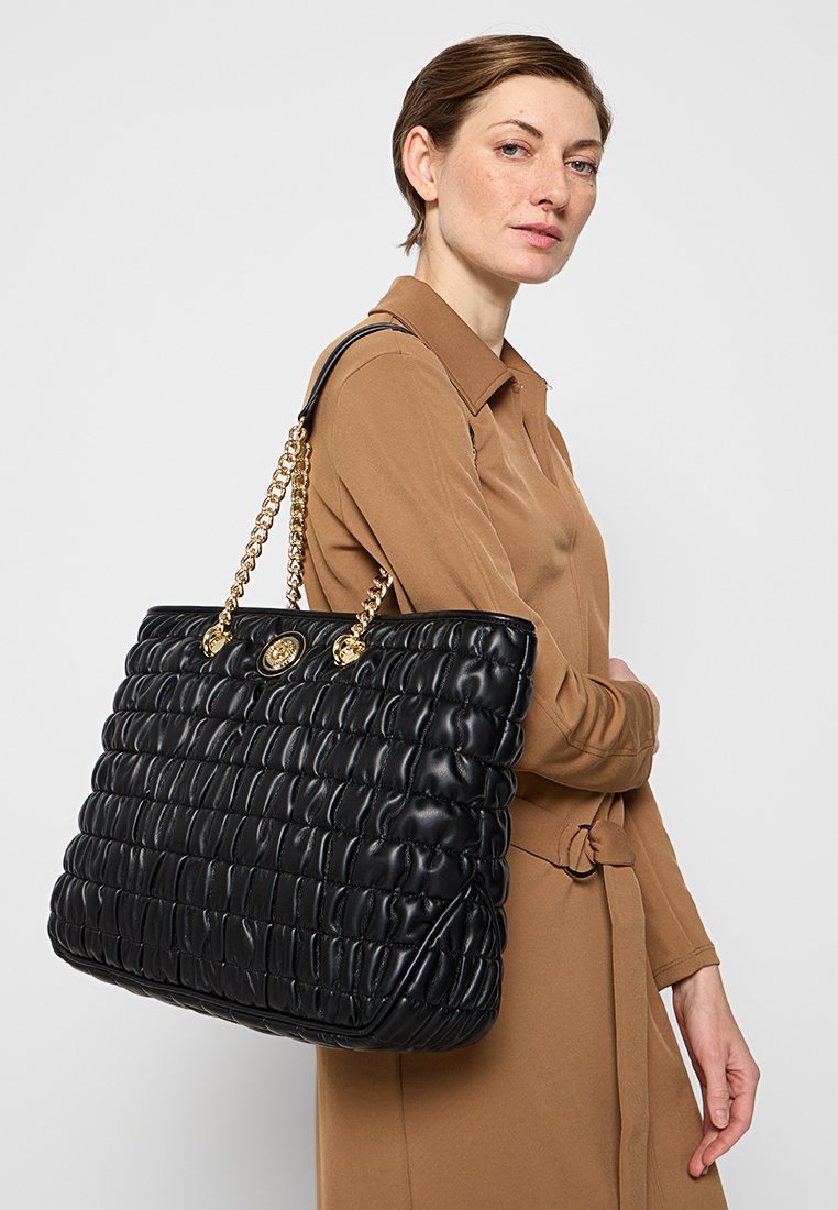 Borsa tote trapuntata nera con hardware dorato e manici a catena. Superficie texture e forma rettangolare, adatta per un uso quotidiano.