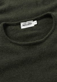 Dunkelgrüner Wollpullover mit Rundhalsausschnitt und weicher Textur. Etikett sichtbar mit Markennamen "hessnatur" und Größe "S."