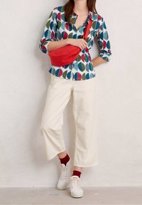 Colorful leaf-patterned shirt in blue, green, and red, white background; paired with cream wide-leg pants and red-accented sneakers. Red bag.