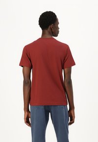 Camiseta de algodón burdeos de manga corta, cuello redondo y corte relajado. Textura suave, diseño liso, sin patrones ni acentos visibles.
