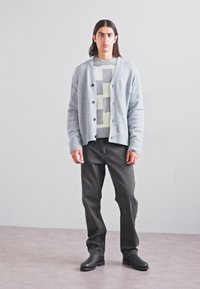 Lichtgrijze cardigan over een gemêleerd grijs en crèmekleurig truitje, gecombineerd met donkergrijze jeans en zwarte enkelboots. Casual pasvorm, gestructureerde stof.