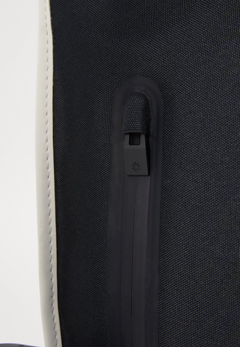 Un tissu texturé foncé avec un tirette de fermeture éclair noire et un cordon en boucle. Le bord est orné d'une finition contrastante de couleur claire.