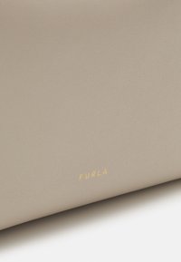 Beige leather wallet with a textured finish. Features gold "FURLA" logo prominently displayed. Simple, sleek design with no visible hardware.