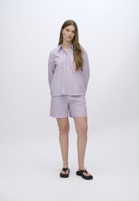 Set di pigiama a righe in rosa e bianco, composto da una camicia con bottoni dotata di taschino e pantaloncini abbinati. Il materiale sembra leggero e morbido.