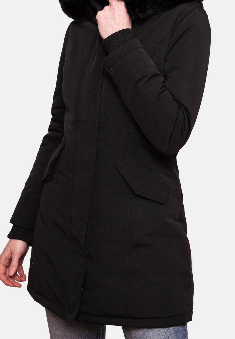 Parka noire avec capuche en fausse fourrure, fermeture éclair, poches latérales et poignets côtelés. Présente une silhouette droite et un tissu texturé.