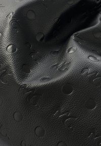 Pelle nera testurizzata con monogramma in rilievo e motivi circolari. La superficie ha una sensazione morbida e leggermente in rilievo.